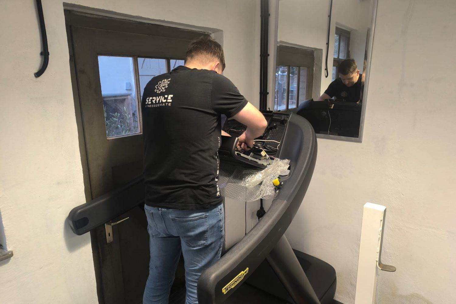 Technicien intervenant sur la console ouverte d’un tapis de course, câblage apparent